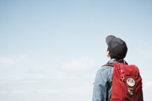 Student with his backpack, back to camera, looking up at blue sky