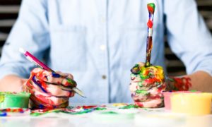 A child sits at a desk with paint on their hands