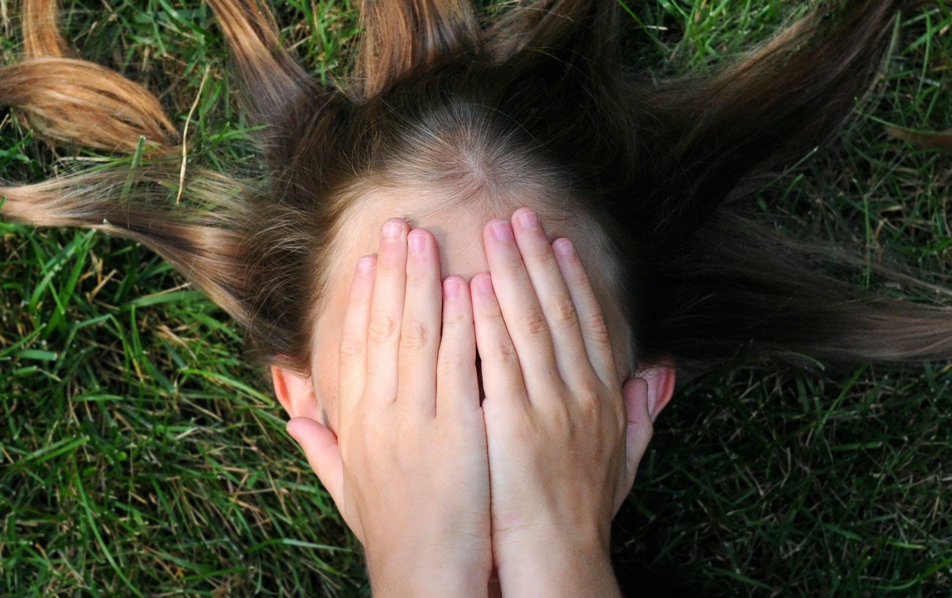 Focus on a child's face as she lays on grass, her hands covering her face