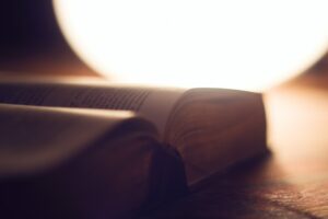 A round lamp illuminates a thick book laying open on a desk